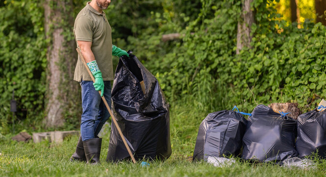 Cleaning up the forest. Putting trash in garbage bag, environmental protection. Volunteer helps to pick up garbage. Pollute forest. Eco-conscious man. Planet pollution environmental protection - Powered by Adobe