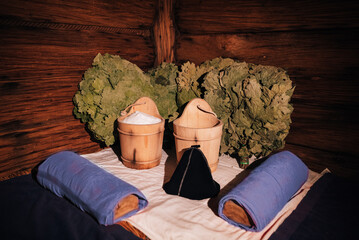 Sauna accessories with oak brooms, wooden buckets and towels inside wooden steam room