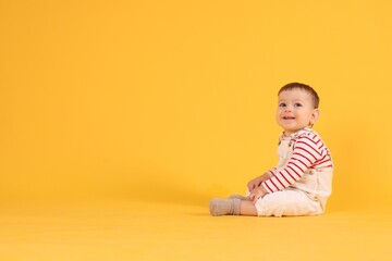 Naklejka premium Cute little baby sitting on yellow background, space for text