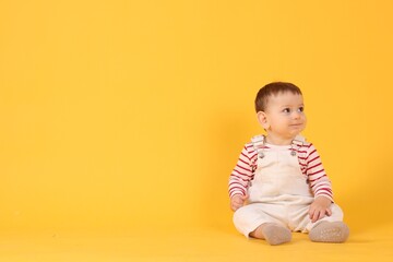 Naklejka premium Cute little baby sitting on yellow background, space for text
