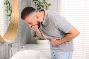Fototapeta premium Man suffering from stomach ache and nausea over sink in bathroom