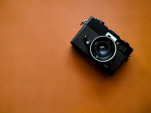 Black vintage camera with textured grip positioned on a brown background. 