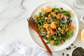 Roasted pumpkin quinoa salad with arugula and chickpeas in a plate with fork on white kitchen table. Top view. Copy space.