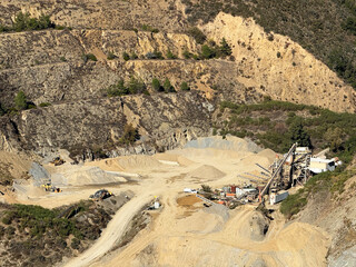 Aerial view of industrial quarry embedded in rugged hills representing environmental change, human industry, and geological layers shaped by resource demand and terrain alteration.
