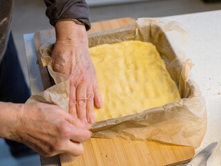Hands preparing dough in baking dish on wooden cutting board