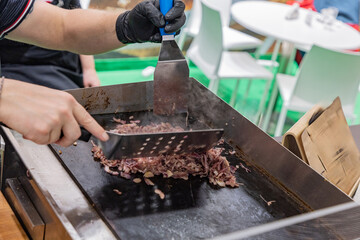 Chef preparing delicious grilled meat on hot griddle with smoke rising