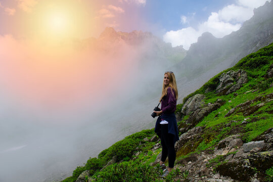 Young and beautiful photographer girl poses in a grassy field in the mountains..