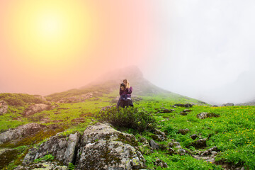 Young and beautiful photographer girl taking photos with professional camera on a grassy field in the mountains..