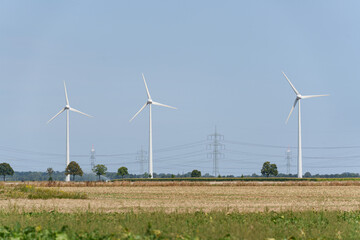 Row of wind turbines aligned across farmland with power lines in the distance near Dusseldorf, Germany