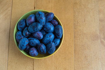 Blue plums in a bowl on a wooden table, copy space