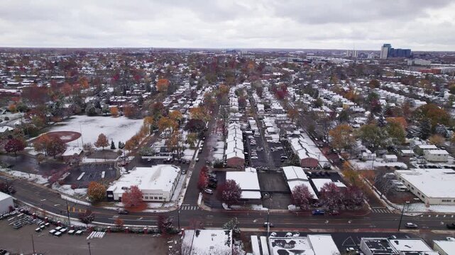 Drone shot and aerial view of Columbus, Ohio neighborhood homes, buildings, roads, buildings, and businesses during late fall after winter snowfall snow falling and colorful autumn trees and leaves up