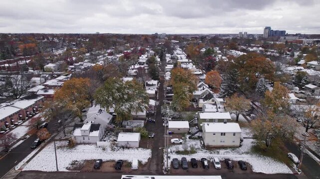 Drone shot and aerial view of Columbus, Ohio neighborhood homes, buildings, roads, buildings, and businesses during late fall after winter snowfall snow falling and colorful autumn trees and leaves up