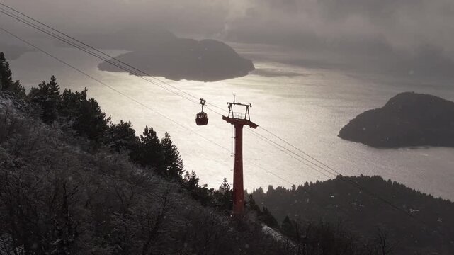 Cable car moving over snowy forest with Nahuel Huapi Lake and mountains in the background, Bariloche, Argentina.