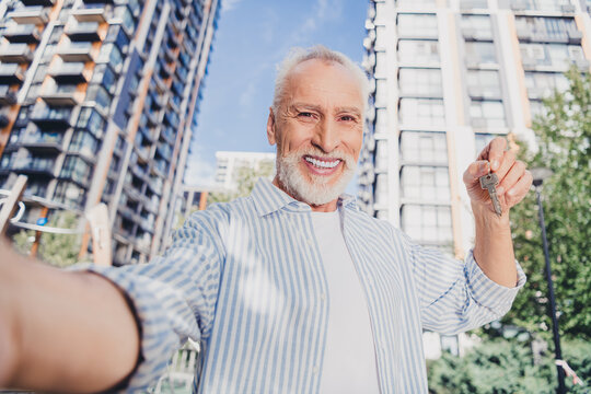 Smiling elderly man holds keys in front of modern city apartments outdoors under bright summer sun in a lively urban setting for real estate lifestyle stock photography
