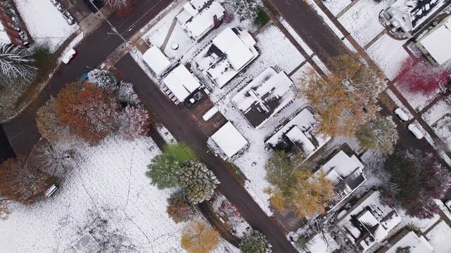 Drone shot and aerial view of Columbus, Ohio neighborhood homes, buildings, roads, buildings, and businesses during late fall after winter snowfall snow falling and colorful autumn trees and leaves up
