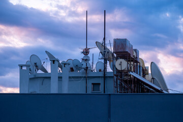 evening Blue sky, Crowded urban rooftop with satellite dishes, antennas, and water tanks against dramatic twilight sky, modern connectivity, city life, technological clutter, communication technology