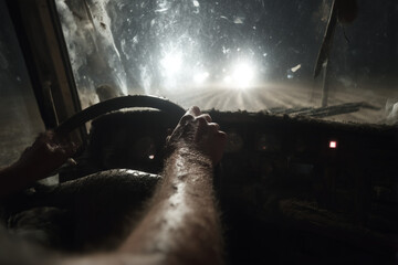 Truck driver steering wheel at night through dusty road with headlights shining ahead. Concept of transportation, logistics, hard work, endurance and night driving. Realistic cinematic lighting from 
