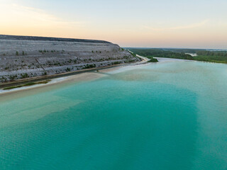 Aerial view of turquoise waters of Auvere ash pond near Narva, Estonia, with rippled surface, quarry landscape, and greenery at sunset.
