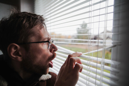 Angry man in glasses peeking through window blinds. Spying on the neighbors. Problems with the neighborhood.