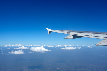 An airplane wing extends into a bright blue sky filled with soft white clouds, capturing the serene beauty of air travel on a sunny day