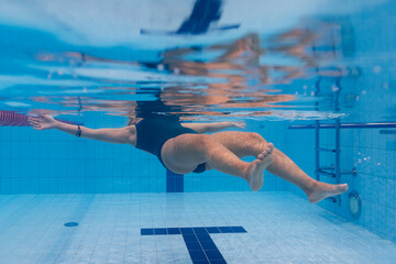 Underwater view of a woman in a swimsuit swimming on her back in a clear blue pool.