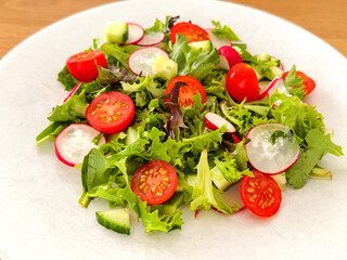 Close up view of a simple salad with lettuce, tomatoes, cucumber and radish on a white plate