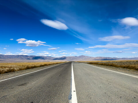 Desert highway stretches to horizon under clear blue sky with scattered clouds distant mountains open landscape evokes freedom travel and adventure - Powered by Adobe