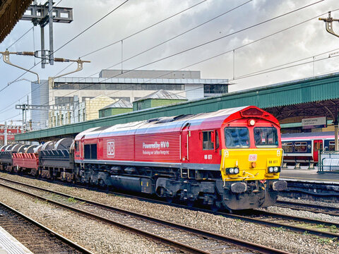 Cardiff, Wales, UK - 24 October 2025: Class 66 freight locomotive (66 077) operated by DB Group pulling a train of wagons carrying heavy steel coils through Cardiff Central Railway Station