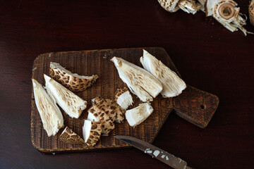 Macrolepiota procera, the parasol mushrooms, freshly sliced to reveal fibrous texture on a dark board. Concept of food preparation, natural pattern, rustic kitchen background. © Natallia