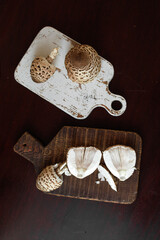 Vertical shot of Macrolepiota procera, the parasol mushrooms, placed on white and brown boards. Concept of rustic color contrast, food styling, and organic composition. © Natallia