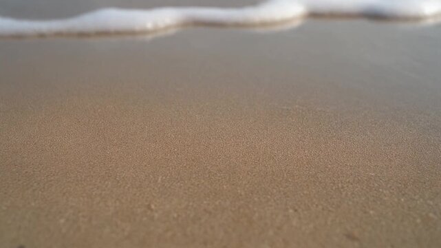 Close-up view of wet sand on a beach with a gentle wave and sea foam.