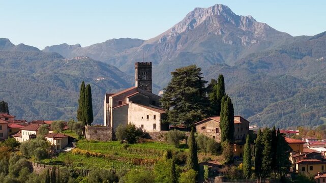 Cinematic 4K aerial view of Barga medieval hilltop town, San Cristoforo Cathedral and Apuan Alps. Tuscany, Garfagnana region, Italy.