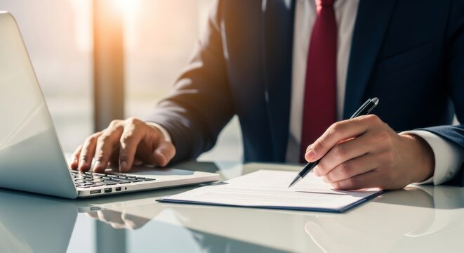 Businessman working on laptop and signing document in modern office