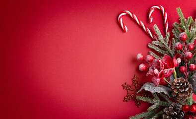 Christmas red background with poinsettia, decorative fir branch and snowflakes, candy canes and cones for tree decoraton. New Year winter holiday composition with decor and copy space, top view.