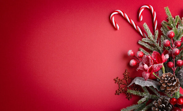 Christmas red background with poinsettia, decorative fir branch and snowflakes, candy canes and cones for tree decoraton. New Year winter holiday composition with decor and copy space, top view.