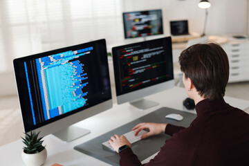 Programmer working on computer with dual monitors at white table in office