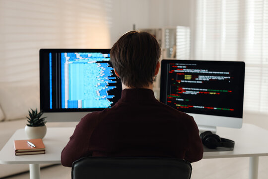 Programmer working on computer with dual monitors at white table in office, back view