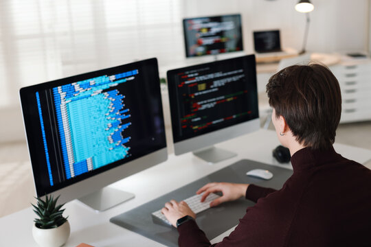 Programmer working on computer with dual monitors at white table in office