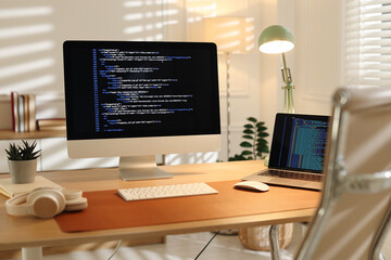 Programmer's workplace with computer, laptop and headphones on wooden table in office