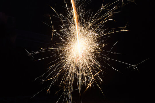 Sparkler Firework. Close-up of a bright sparkler emitting golden sparks against a dark background. - Powered by Adobe