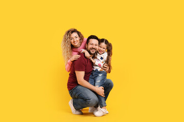 Happy parents and their daughter hugging on yellow background. Family bonding