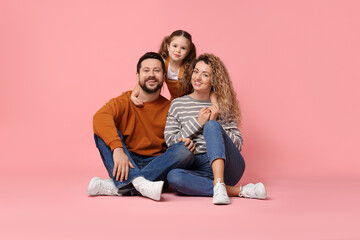 Happy parents and their daughter hugging on pink background. Family bonding