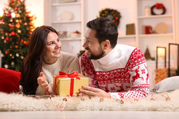 Happy couple with gift box spending time together in room decorated for Christmas