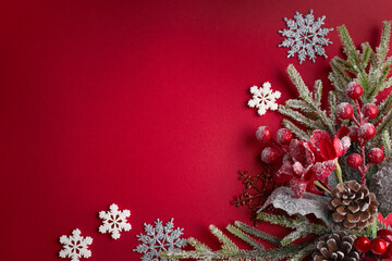 Christmas red background with decorative poinsettia, fir branch, snowflakes and cones for tree decoraton. New Year winter holiday composition with decor and copy space, top view.