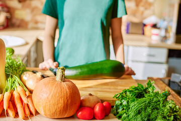 Ripe autumn vegetables on a wooden table with space for a copy, cook in the background. Making a holiday Thanksgiving dinner, ripe fall harvest from the garden. Pumpkin, ripe carrots, tomatoes