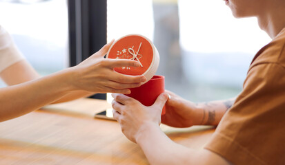 A guy gives a girl a gift in a red box, hands open the box. Female and male hands with gift close-up, space for copy, text and advertisement. Birthday, Valentine's Day, February 14, Wedding