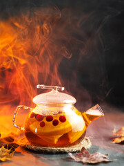 Fruit tea with berries in a glass teapot. A hot, warming drink. Dried autumn leaves and spices. Steam from the hot drink.