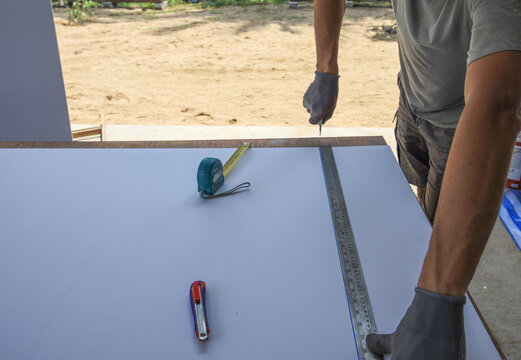 Man is measuring a piece of wood with a tape measure and a ruler