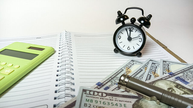 A desk setup showing a small clock, calculator, pen, and dollar bills on a notebook, symbolizing financial planning, budgeting, and effective time management in business or personal finance.
