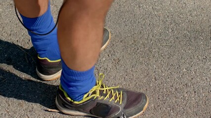 runner preparing outdoors, athletic man tying shoes outside, closeup of male runner fixing laces during morning jog, focused male runner in blue socks preparing for exercise on sunlit asphalt path